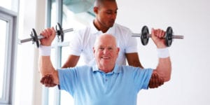 Caregiver Assisting Elderly Man Carrying Dumbells