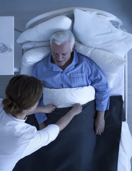 Nurse supporting elderly man in bed for overnight in-home care